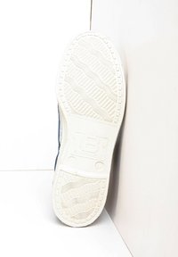 Semelle de sneaker en caoutchouc blanc texturé, avec un motif en vagues subtil et un marquage en relief. Le côté est bleu marine avec des accents de couture clairs.