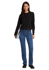 Top corto negro de manga larga con detalles metálicos, combinado con jeans de mezclilla azules (acampanados) y botas de tobillo negras con suela gruesa, llevando un bolso plateado.