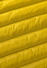 Tissu matelassé jaune avec une texture légèrement brillante, présentant des coutures verticales et des motifs linéaires subtils dans tout le tissu.