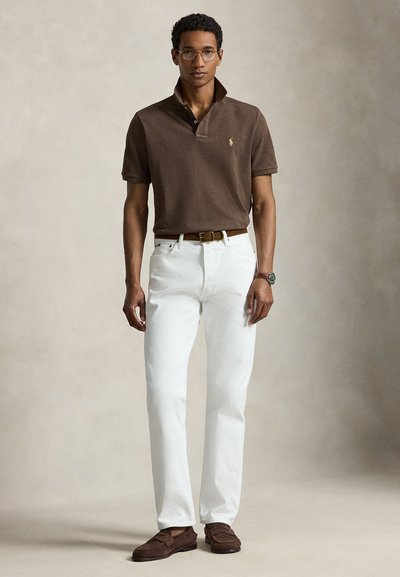 Mees kannab pruuni polosärki üles keeratud krae, valgeid teksasid, pruuni vööd, pruune mokasiine, prille ja kella, seisab neutraalse taustaga ees.