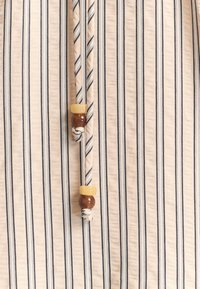 Beige stof met zwarte verticale strepen, met een gebonden koord met houten kralen—één gele en één bruine—aan het uiteinde.