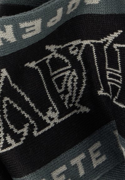 Melnas un pelēkas adītas audums ar lieliem, izsmalcinātiem gotikas stila burtiem un mazāku blokveida tekstu gar malām.