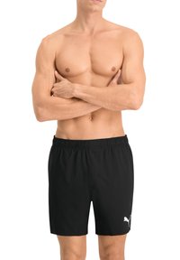 Fekete sportnadrág elasztikus derékrésszel és kis fehér Puma logóval. Könnyű anyag, testhezálló fazon és combközép hosszúság.