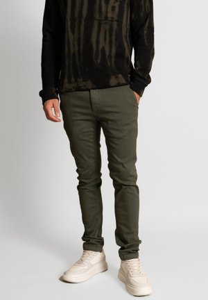 Olive green chinos with a slim fit in cotton fabric, featuring a standard pocket design and pair with cream-colored sneakers.