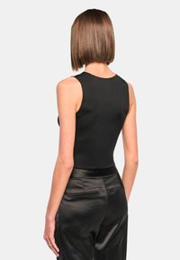 Black fitted tank top with a round neckline, sleeveless design, and smooth texture, paired with tailored black satin pants featuring back pockets.