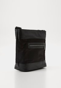 Borsa nera in nylon con dettagli in pelle, dotata di una tasca con zip sul davanti, forma strutturata e tracolla regolabile.