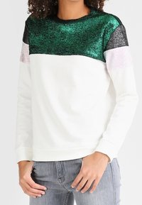 Sudadera blanca con la parte superior decorada con un patrón brillante en verde, negro y rosa. Mangas largas con puños acanalados, textura de tela suave.