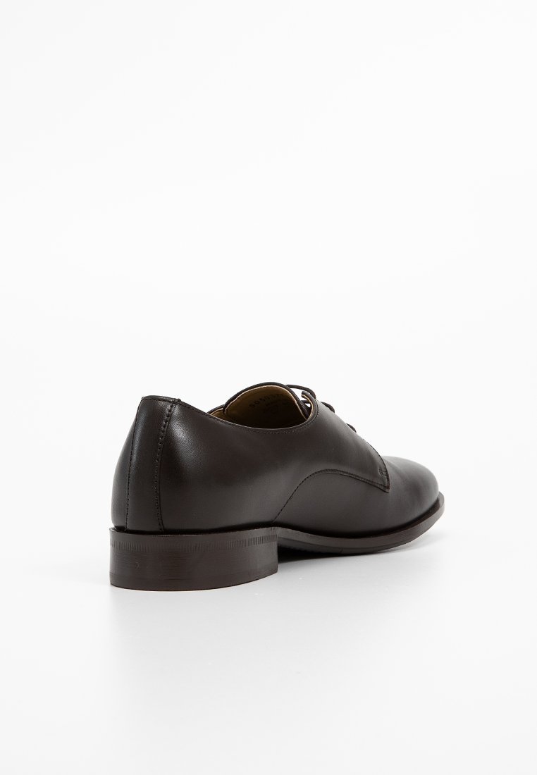 Chaussure habillée en cuir marron avec une finition lisse, un bout arrondi, un petit talon et un laçage. Couture visible sur les côtés.