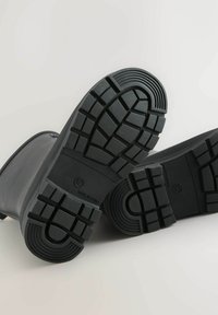 Bottes en caoutchouc noires avec une semelle texturée et crantée. La semelle comporte de profondes rainures pour une meilleure adhérence et inclut un marquage du fabricant.