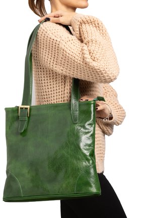 Groene leren totebag met een glanzende afwerking, rechthoekige vorm, dubbele handvatten en een gespaccent. Gedeeltelijk gedragen tegen een gestructureerde trui.