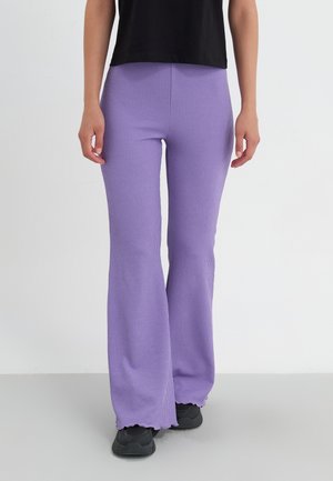 Paarse geribbelde flare broek van zacht materiaal, met een gestructureerde oppervlakte en onafgewerkte zomen. Gecombineerd met zwarte schoenen.