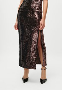 Juoda ir rožių auksu blizgučių sijonas su šonine iškarpa, iki kelių ilgio, aptemptas dizainas, lygus paviršius, derinamas su juodais smailiais aukštakulniais bateliais.