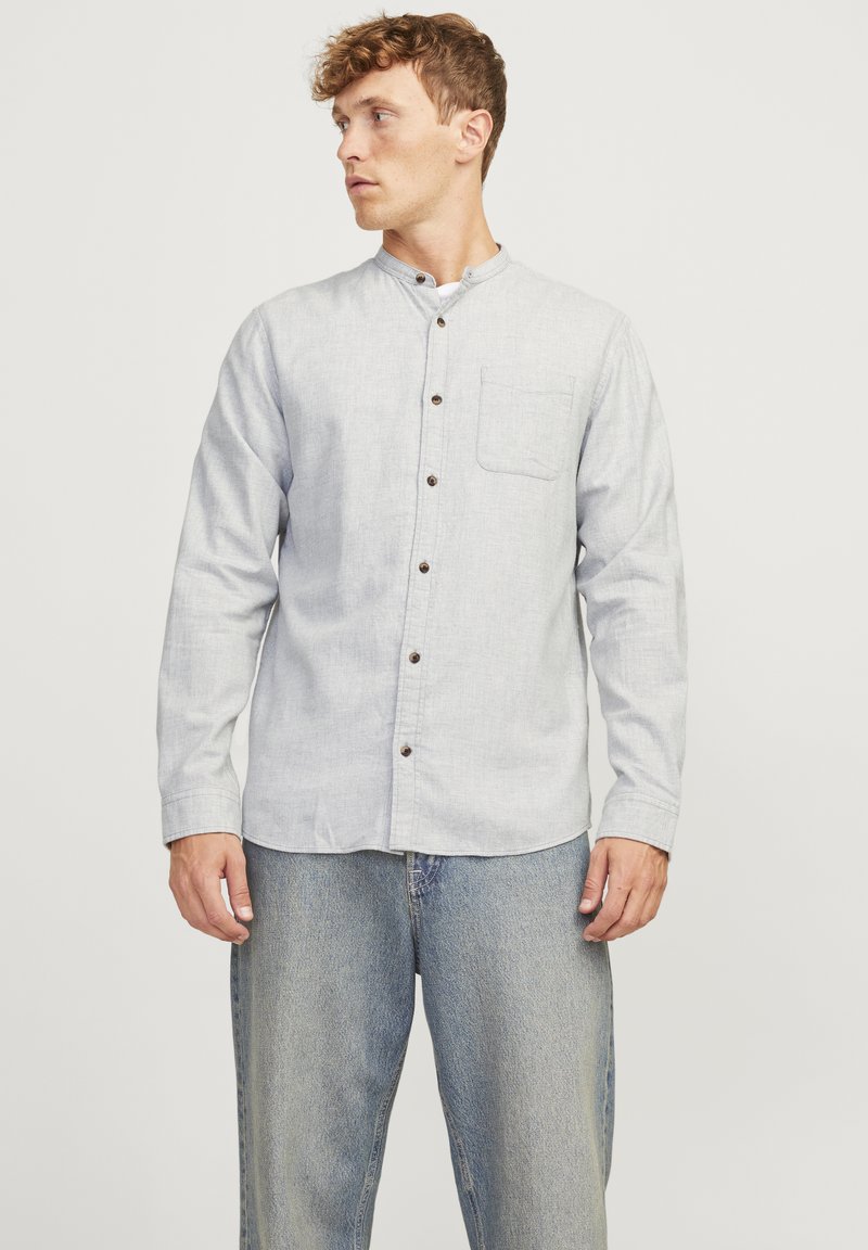 Heled hallikas seletav särk, millel on mandariini krae, üks rinnatasku ja pruunid nööbid; valmistatud tekstureeritud kangast, kitsas sobivus.