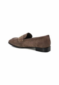 Mocasín de ante marrón con punta redondeada, bajo tacón negro y tachuelas decorativas en tono dorado en la parte superior. Textura suave y diseño minimalista.