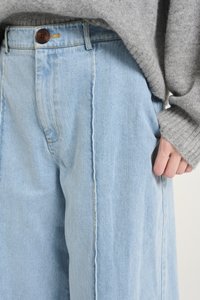 Light blue denim wide-leg trousers featuring a front button closure, visible stitching details, and a relaxed fit.