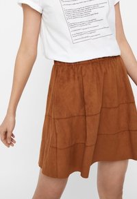 Brauner Wildleder-A-Linien-Rock mit einem gerafften, elastischen Taillenbund und sichtbaren Nähdetails. Die Textur wirkt weich und hat eine matte Oberfläche.