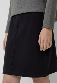 Zwarte rok tot op de knie, gemaakt van een zachte, gestructureerde stof. Heeft een rechte silhouet met subtiele stiknaden langs de zijkanten.