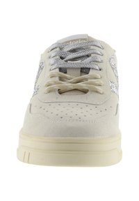 Crèmekleurige suède sneaker met geperforeerde neus, beige en grijze veters, en dikke crèmekleurige zool, vanaf de voorkant gezien.
