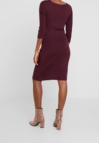 Robe tricotée bordeaux à manches trois-quarts. Présente une silhouette ajustée et un col rond. Associée à des bottines à imprimé serpent.