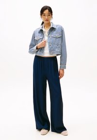 Beskaftet blå- og hvitstripet denimjakke, hvit skjorte med krage, marineblå vide bukser, beige vevde sko. Enkelt design med klassiske farger.