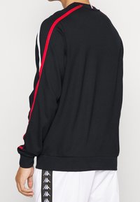 Felpa nera con maniche lunghe, con strisce rosse e bianche sulle spalle e polsini elasticizzati. Realizzata in un tessuto liscio.