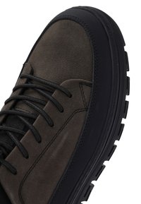 Chaussure en cuir marron foncé avec un bout rond noir, des lacets noirs, et une semelle épaisse noire avec des rainures profondes pour une meilleure adhérence.
