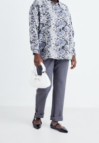 Blå och grå mönstrad oversized blus, grå byxor, svarta lägenheter och en liten vit handväska med spänne.