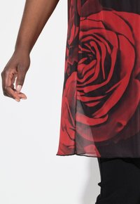Tunika trasparente con un grande motivo di rose rosse su uno sfondo nero. Il tessuto è leggero e fluido, con un orlo che finisce all'altezza dell'anca.