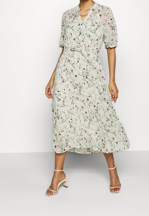 Kwiecista sukienka do kolan w jasnobeżowym kolorze z zielonymi i czarnymi wzorami. Miękka tkanina, krótkie bufiaste rękawy oraz dekolt w kształcie litery V.