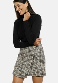 Čierny rolák s dlhými rukávmi, skombinovaný s sukňou po kolená z texturovaného tweedu v čiernych, krémových a šedých odtieňoch.