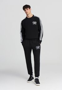 Felpa nera con strisce bianche, girocollo e stampa "New Jersey East Coast". Pantaloni jogger neri con stampa coordinata e polsini elasticizzati.