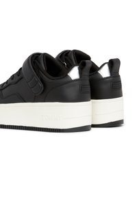 Paire de baskets basses noires avec semelles blanches épaisses, cols rembourrés, bandes Velcro et languettes au talon.