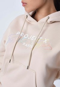 Beige hoodie gemaakt van een zachte katoenmix, met een voorzak, trekkoorden en multicolored logo tekst.