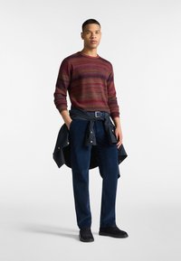 Červený a námornícky pruhovaný sveter, tmavomodré kordové nohavice a námornícka bunda zviazaná okolo pása. Čierne topánky dokončujú outfit.
