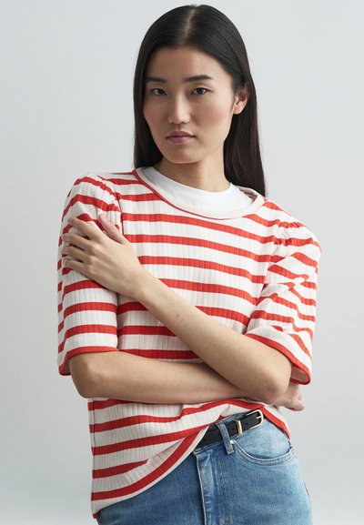 Rot-weiß gestreiftes kurzärmeliges Strickoberteil mit ribbeliger Textur, kombiniert mit blauen Jeans und einem schwarzen Gürtel.