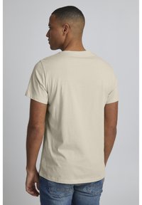 Lys beige bomull t-skjorte med korte ermer og rund hals, vist fra baksiden. Brukt med blå denimjeans.