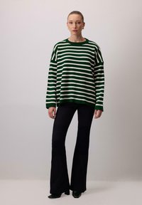 Green and white striped knit sweater with dropped shoulders, paired with black flared pants and green pointed shoes. Smooth texture.