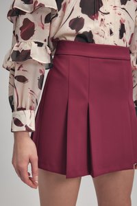 Bordeaux-rode geplooide rok van gladde stof, met een aansluitende tailleband. Gecombineerd met een blouse met een patroon en volants aan de mouwen.