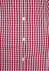 Punainen ja valkoinen ruudullinen paita, jossa on nappikiinnitys valkoisilla napeilla ja sileä puuvillakangas, esitellen klassista gingham-kuviota.