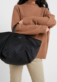 Czarna torba na ramię wykonana z teksturowanego materiału z delikatnym wzorem, z dwoma mocnymi uchwytami i wytłoczonym na przedzie logo marki "JOOP".