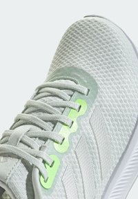 Gros plan d'une basket grise en maille avec des lacets blancs, un panneau d'œillets vert clair et trois bandes texturées sur le côté.