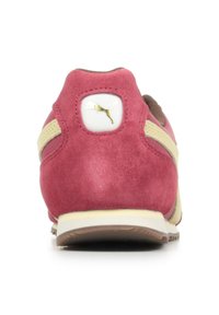 Sneaker in suede rosso con accenti beige e una patch bianca con logo sul tallone. Presenta una suola testurizzata e una forma arrotondata.