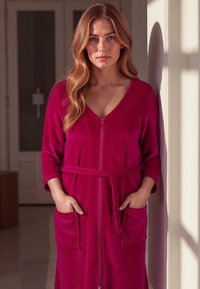 Robe fucsia con zip, maniche tre quarti, tessuto texturizzato, tasche frontali e cintura coordinata, ambientata in uno sfondo interno.