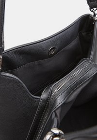 Fekete bőr kézitáska belső tere sima textúrával, cipzáras zsebbel és patentos záródással, egyszerű, funkcionális dizájnal.