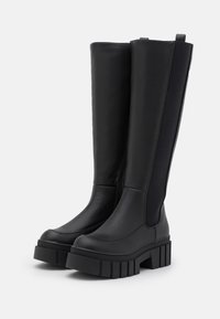 Knöchelhöhe schwarze Stiefel aus glattem Leder mit elastischen Seiten, ausgestattet mit einer dicken, quadratischen Plattformsohle mit rippiger Struktur.