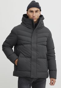 Puffer jacket in dark gray with a high collar, horizontal quilted pattern, and dual zippered side pockets. Worn on a person.