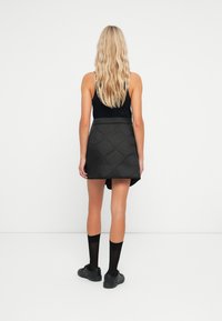 Jupe mini matelassée noire avec une taille ajustée et un ourlet arrondi, portée avec un haut sans manches noir, des chaussettes jusqu'aux genoux et des chaussures noires.
