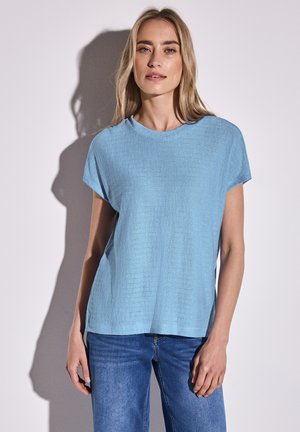 Top azzurro chiaro a maniche corte con una vestibilità leggermente ampia e scollo rotondo, abbinato a jeans in denim blu.