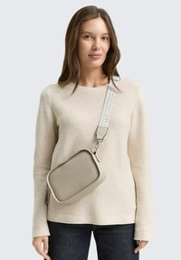 Beige Umhängetasche mit einer glatten Textur und rechteckiger Form; verfügt über einen gemusterten Schulterriemen und silberne Metallakzente.