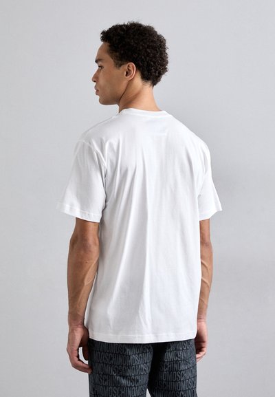 T-shirt en coton blanc à manches courtes et encolure ronde, vu de dos. Associé à un short à motifs sombres.